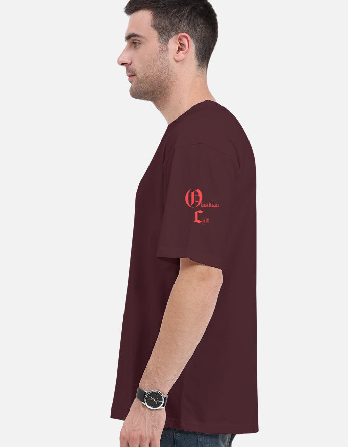Man wearing burgundy loose fit t-shirt with red Oldskullair logo on left shoulder, light background